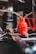A red oil can with a metal spout and handle is surrounded by various tools, including a wrench and what appears to be a piece of metal with holes. The background is blurred, focusing attention on the oil can and tools, suggesting a workshop or garage setting.