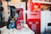 Several car care products, including bottles of wax and detailing spray, are placed on a soft cloth in a garage setting. A red tool chest stands in the background, slightly out of focus, against a backdrop of shelves and storage areas. The products feature prominent labels and branding.