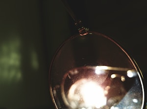 A close-up of a translucent object with a visible fingerprint and light reflections. The background is dark, creating a stark contrast with the illuminated portion.