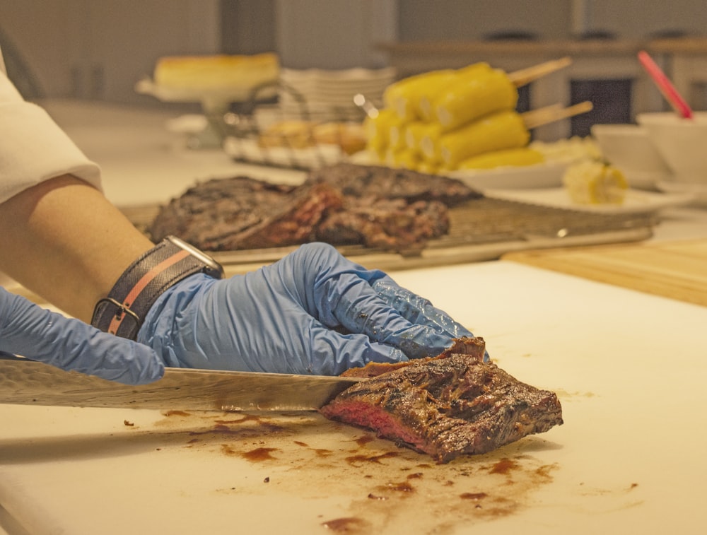 person in grey shirt slicing meat on white chopping board