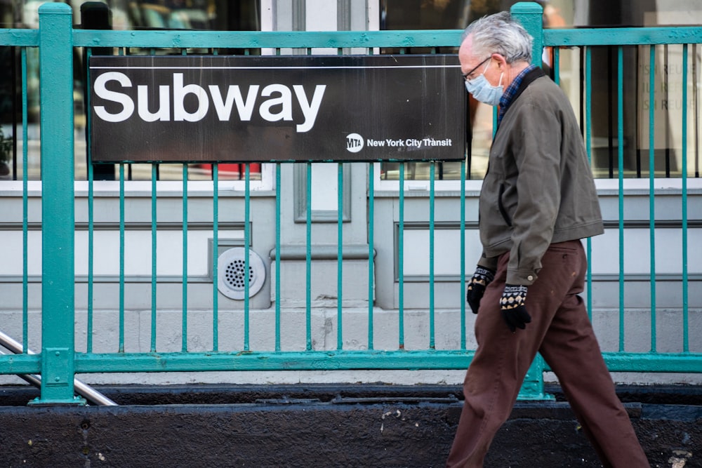 man in gray coat and brown pants standing beside blue steel gate during daytime