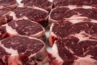 Several raw steak cuts of red meat with marbling are arranged in a neat, overlapping pattern. The meat appears fresh and ready for cooking.