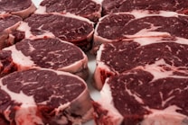 Several raw steak cuts of red meat with marbling are arranged in a neat, overlapping pattern. The meat appears fresh and ready for cooking.