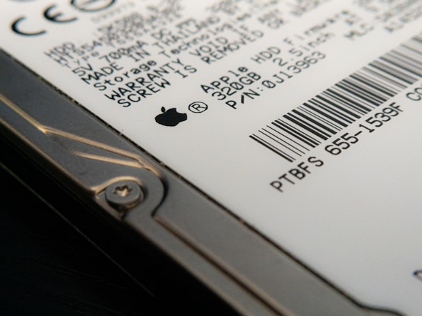 Close-up view of a hard drive with visible text and a barcode. The focus is on the details of the labeling, including technical specifications and a recognizable logo. The image captures the edge of the hard drive with a visible screw.