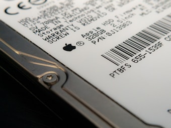 Close-up view of a hard drive with visible text and a barcode. The focus is on the details of the labeling, including technical specifications and a recognizable logo. The image captures the edge of the hard drive with a visible screw.