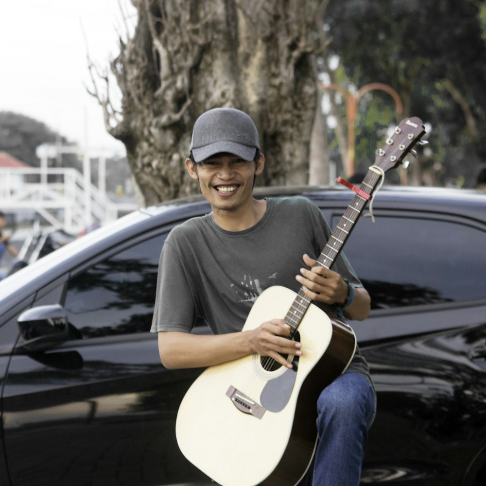 a man sitting on a car holding a guitar