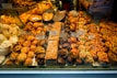 An assortment of pastries and baked goods displayed in a bakery window, including cookies, croissants, and cakes. Each item is labeled with a price tag. The pastries vary in shapes and sizes, with some topped with almonds and others drizzled with chocolate.