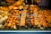 An assortment of pastries and baked goods displayed in a bakery window, including cookies, croissants, and cakes. Each item is labeled with a price tag. The pastries vary in shapes and sizes, with some topped with almonds and others drizzled with chocolate.