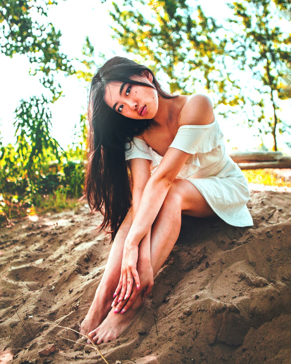 woman in white dress sitting on brown sand during daytime