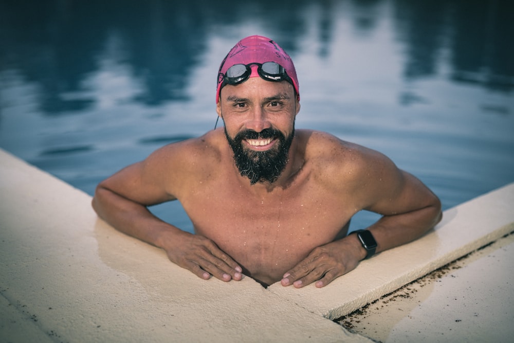 topless man wearing black goggles sitting on white sand during daytime