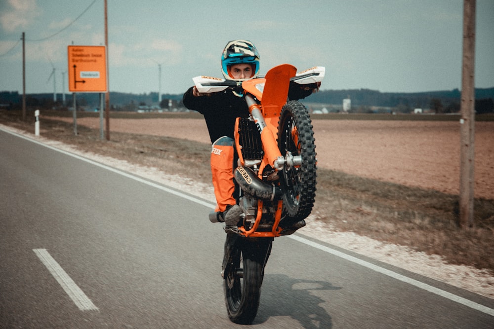 주황색 헬멧을 쓴 남자가 낮 동안 도로에서 오토바이를 타고 있다