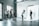 A photography studio scene featuring a photographer capturing a male subject who is posing on a white backdrop. Several people are observed behind the photographer, including a woman adjusting equipment and others casually standing around. The room is industrial-style with large windows and visible vents on the ceiling.