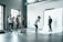 A photography studio scene featuring a photographer capturing a male subject who is posing on a white backdrop. Several people are observed behind the photographer, including a woman adjusting equipment and others casually standing around. The room is industrial-style with large windows and visible vents on the ceiling.