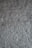 A textured surface of a rough, uneven gray wall. The wall's surface is characterized by a stucco finish with visible bumps and ridges, creating a rustic and tactile appearance.