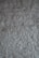 A textured surface of a rough, uneven gray wall. The wall's surface is characterized by a stucco finish with visible bumps and ridges, creating a rustic and tactile appearance.