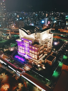 A nighttime cityscape with a high-rise building wrapped in vibrant neon purple and electric cyan 3D projection mapping.