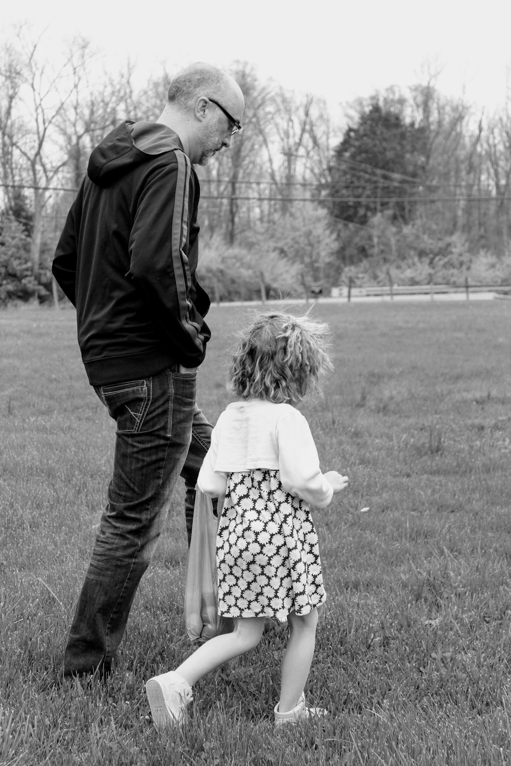 grayscale photo of man and woman walking on grass field