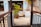 An outdoor area featuring a pathway lined with dark wooden railings leading to a patio with potted plants. The patio shows tiled flooring and steps that ascend on both sides. There is a large potted palm and smaller plants placed around, giving the space a tropical feel.