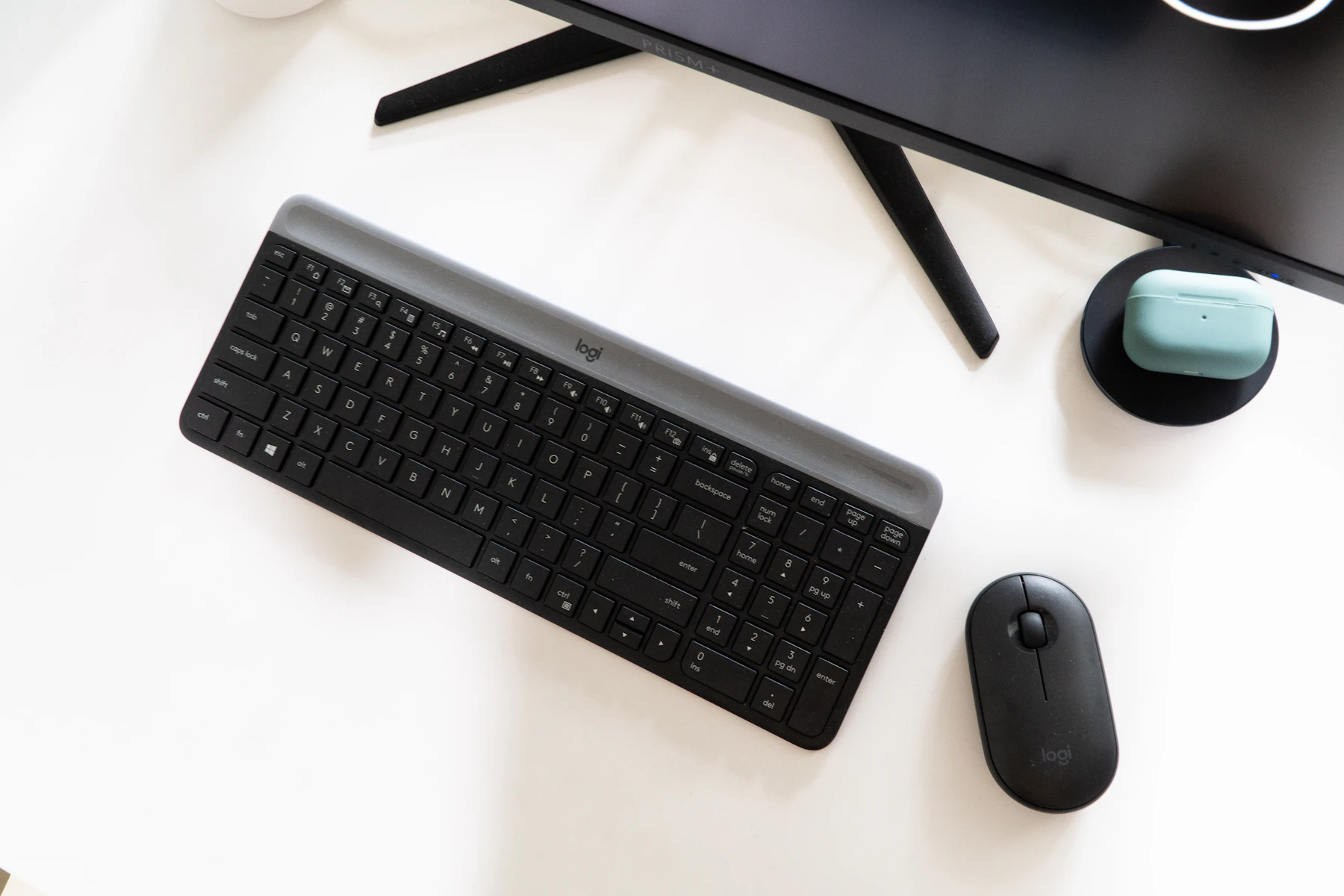 Teclado e mouse sem fio pretos sobre mesa branca, em frente a um monitor