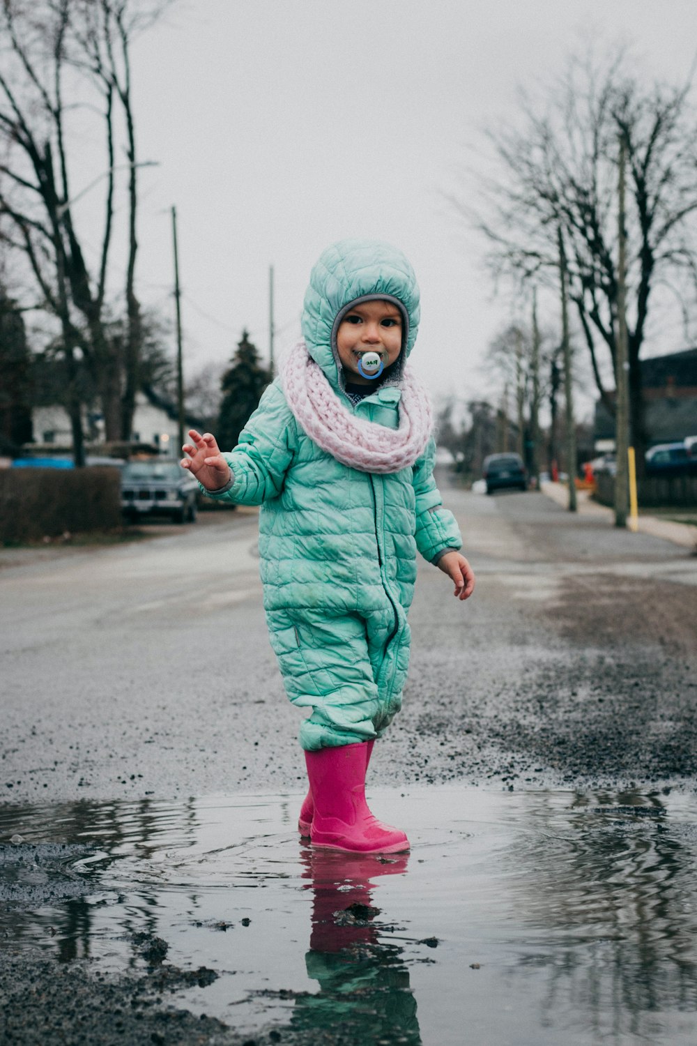 girl in teal jacket and pink pants standing on wet road during daytime