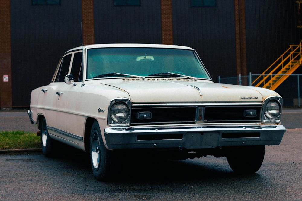 Voiture classique blanche garée près d’un bâtiment brun