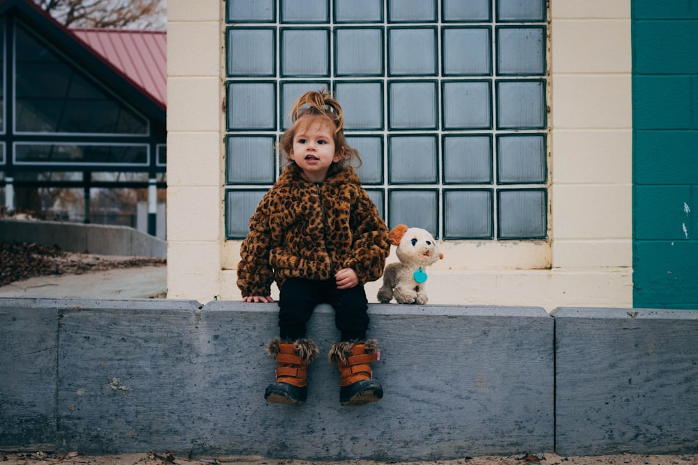 girl in brown and black leopard print coat sitting on gray concrete floor