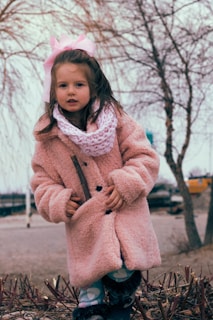 A young girl wearing a cozy winter coat and scarf outdoors.