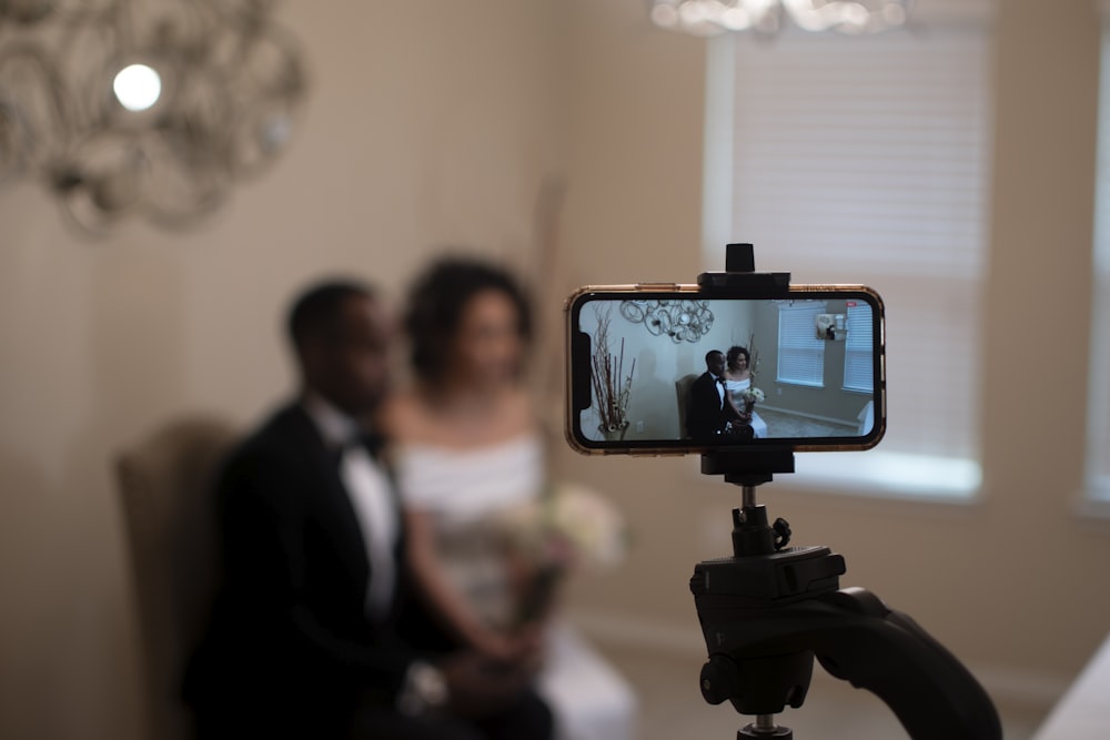 man in black suit taking photo of woman in white dress