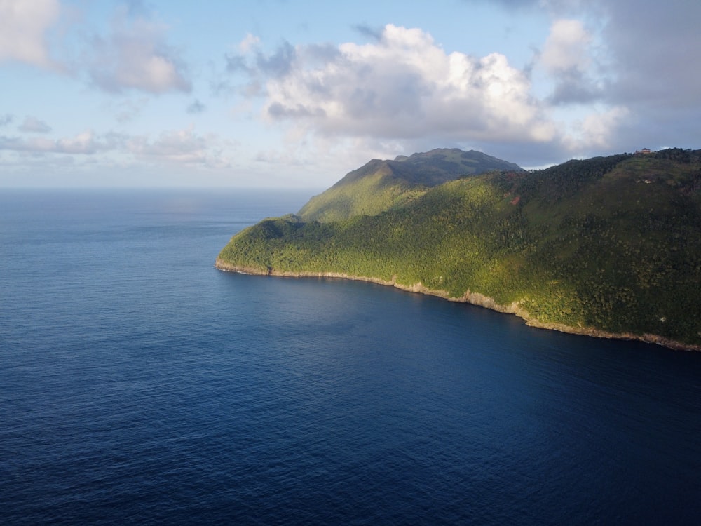 grüner Berg neben blauem Meer unter weißen Wolken und blauem Himmel tagsüber