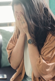 woman in brown shirt covering her face