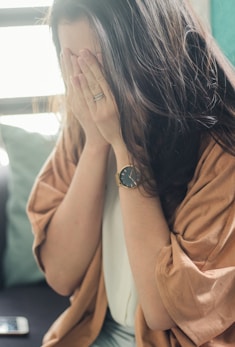 woman in brown shirt covering her face