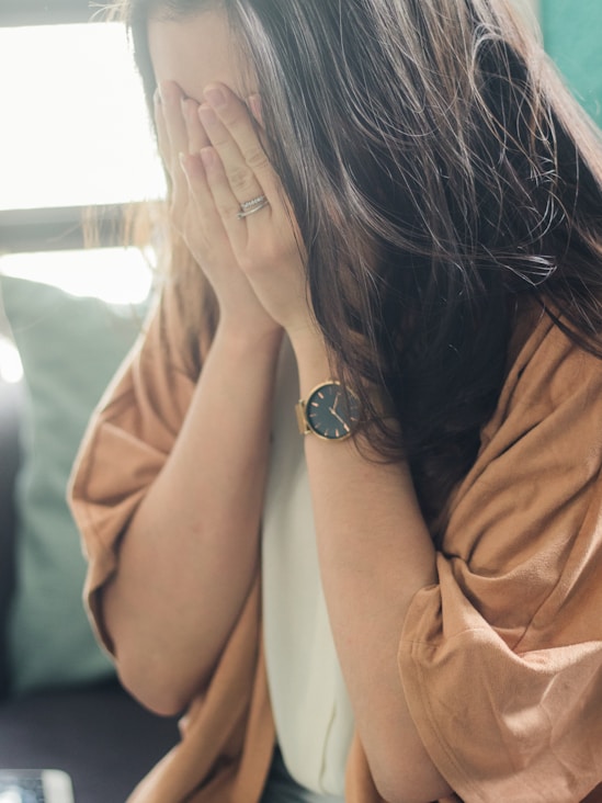 woman in brown shirt covering her face