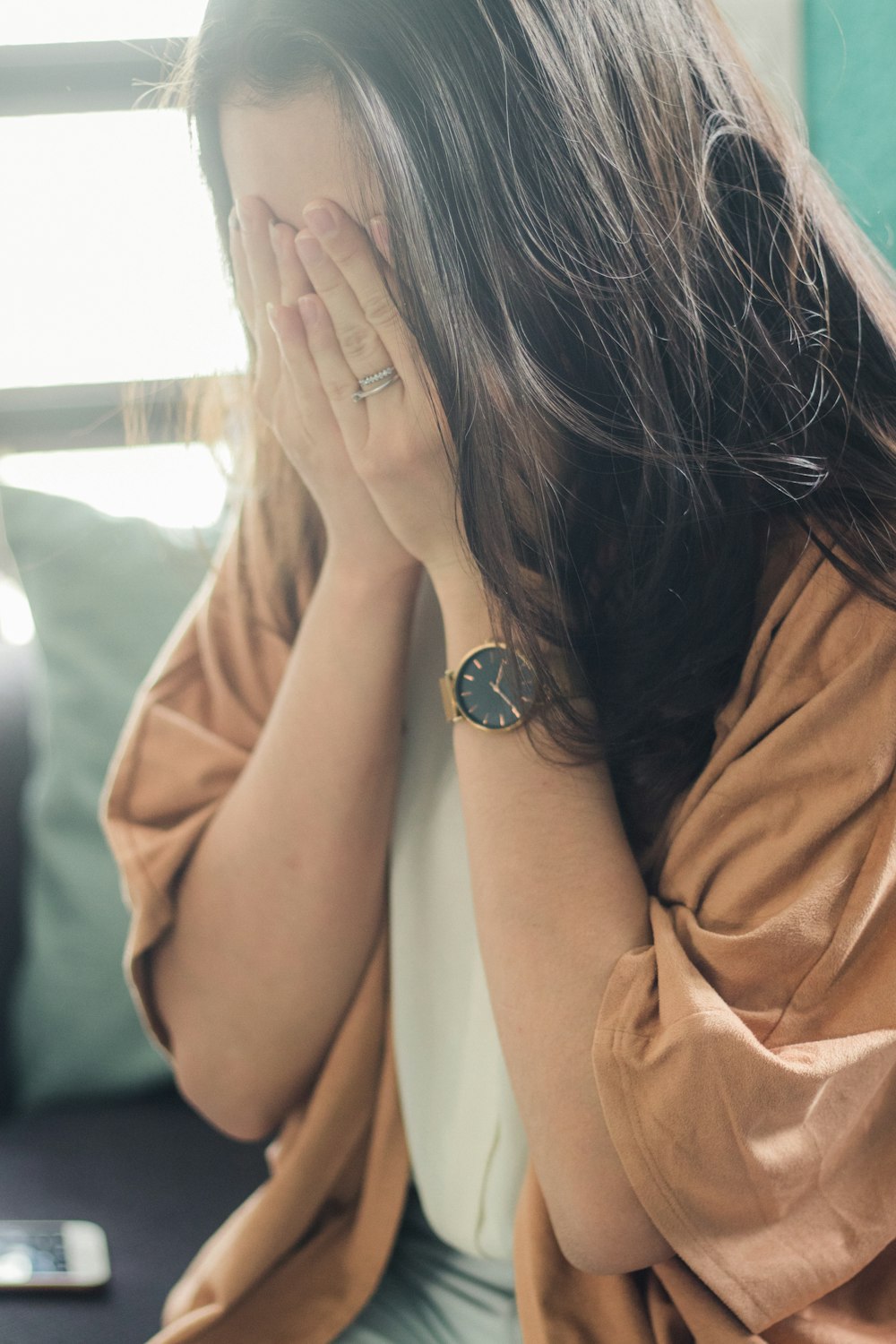 woman in brown shirt covering her face