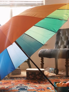 A sleek umbrella stand holding several colorful umbrellas next to a minimalist decorative bowl on a console table.
