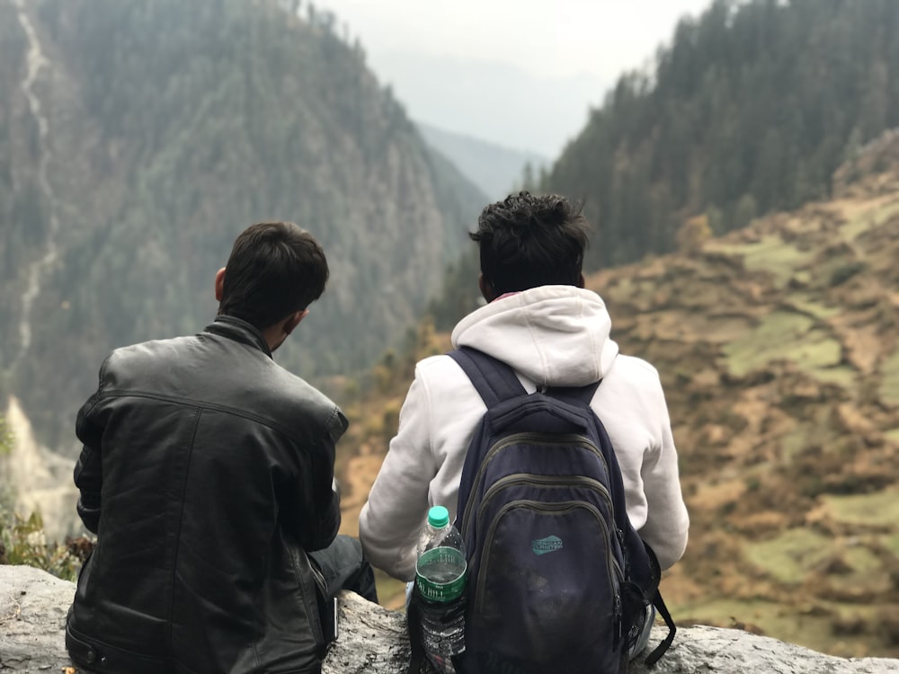 man in black jacket and white backpack sitting on rock during daytime