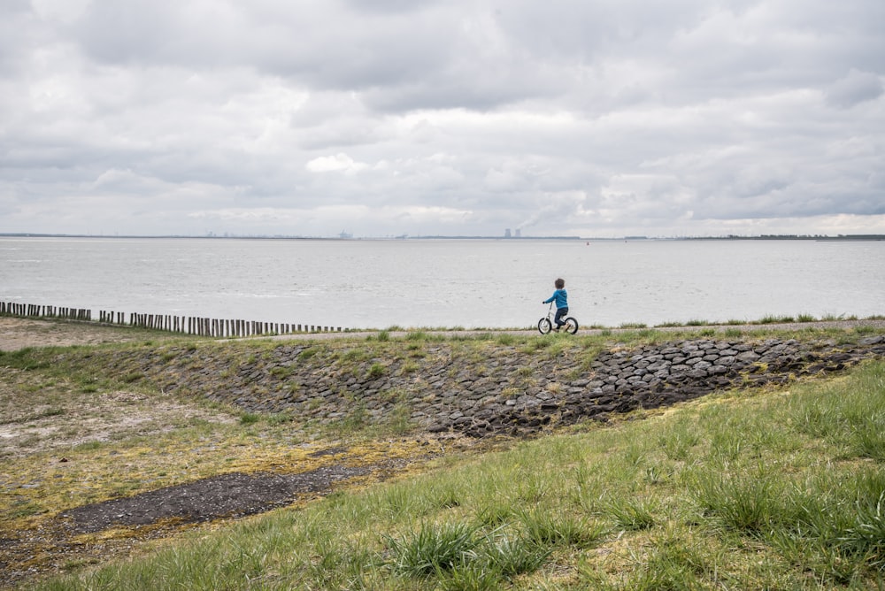 person in blue shirt walking on green grass field near body of water during daytime