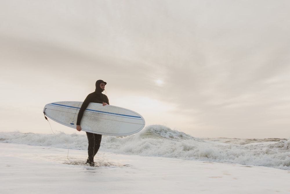 woman in black bikini holding white surfboard standing on white snow covered ground during daytime