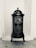 A vintage cast iron stove with ornate detailing, featuring a domed top and two small doors with engraved patterns. It stands against a textured white wall on a wooden floor.