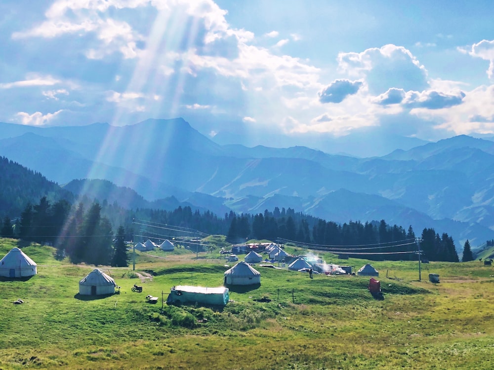 white and blue tent on green grass field near mountains under white clouds and blue sky