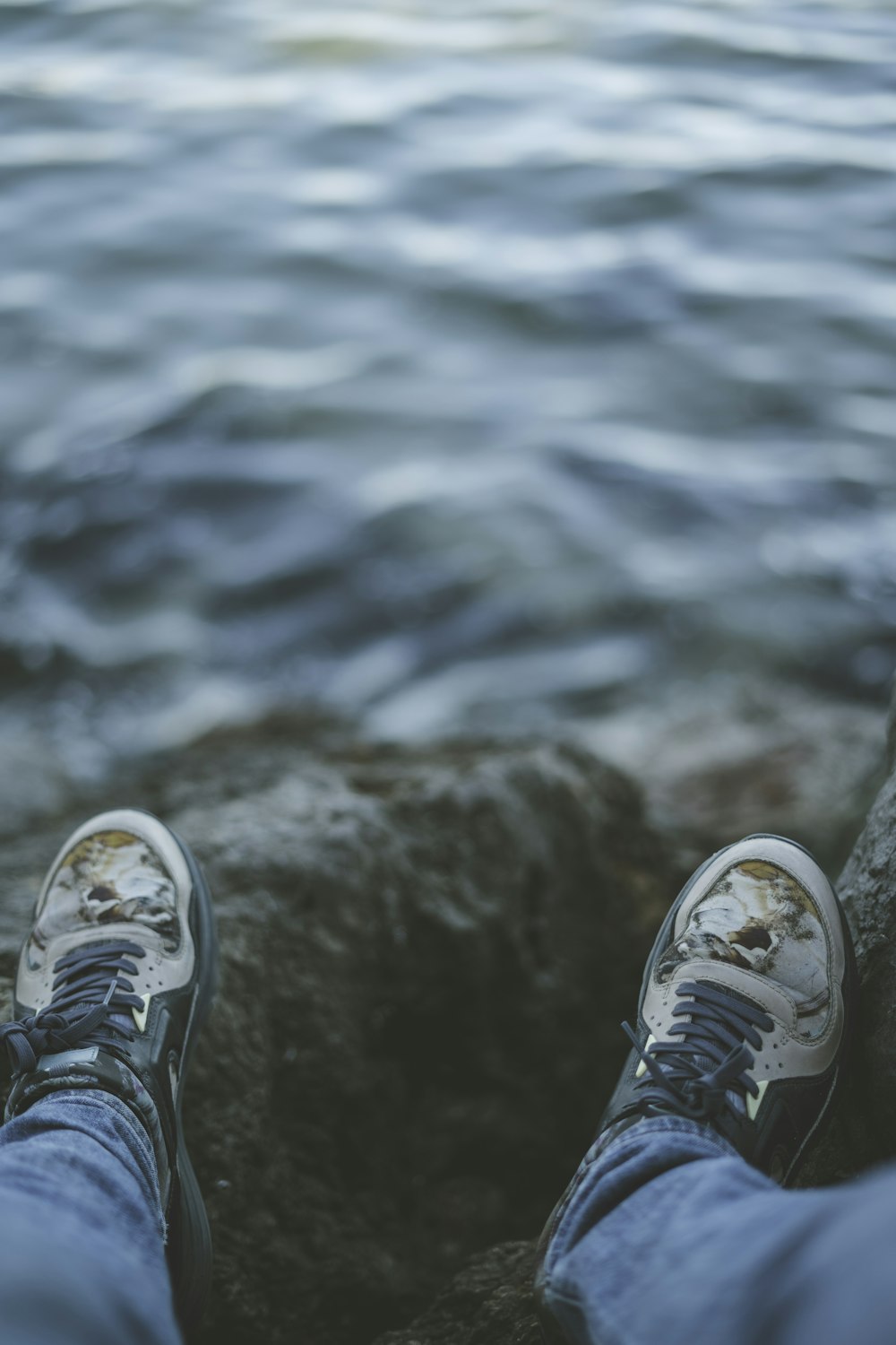 person in gray and white sneakers standing on brown rock near body of water during daytime