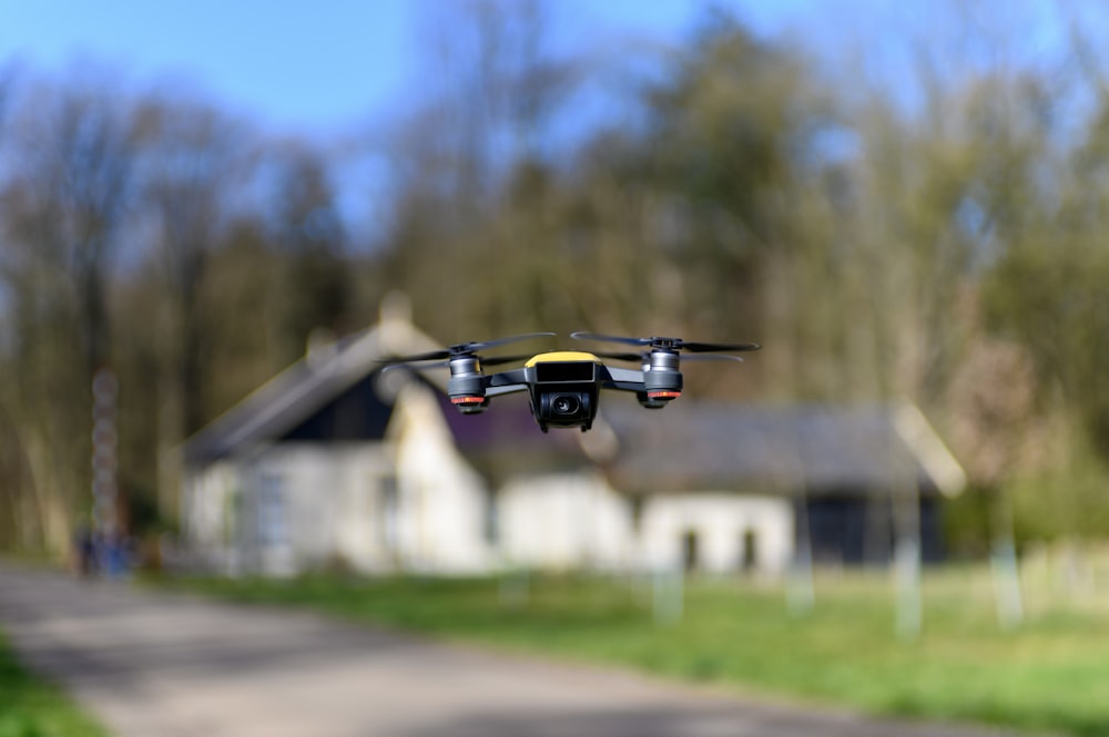 Drone noir et jaune volant au-dessus du champ d’herbe verte pendant la journée