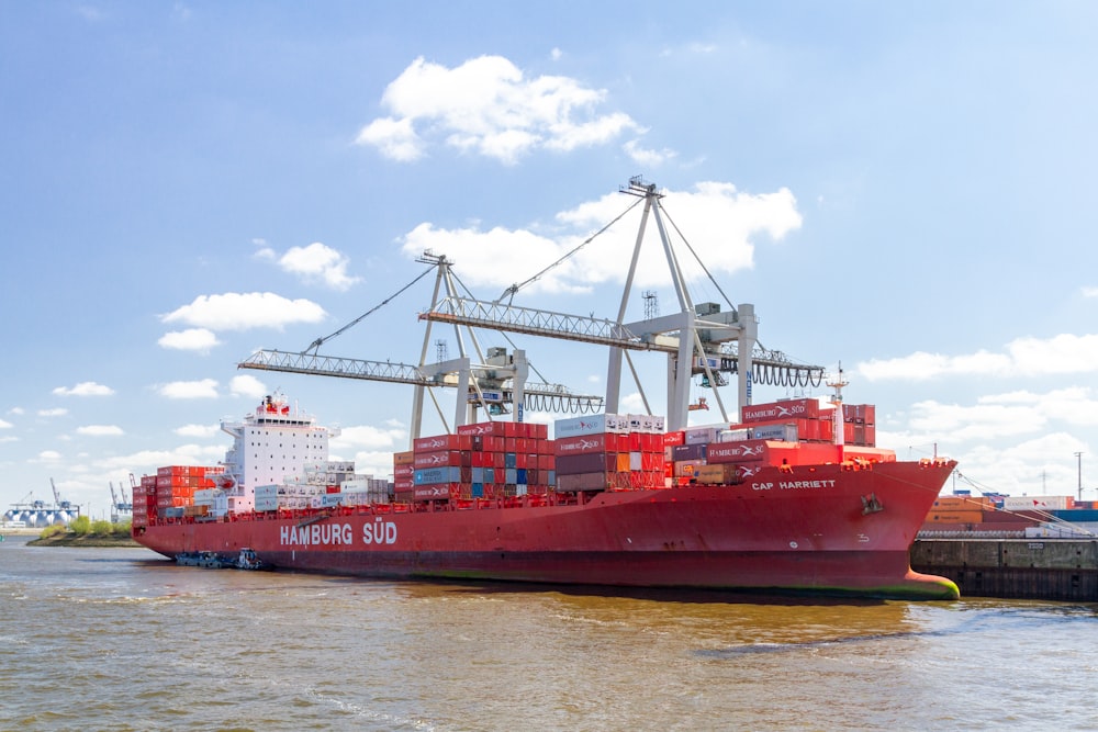 red cargo ship on sea under white clouds and blue sky during daytime