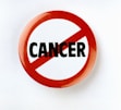 A circular badge with a red border and slash through the word 'CANCER' printed in bold black letters on a white background, symbolizing opposition or prohibition.