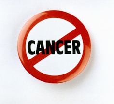A circular badge with a red border and slash through the word 'CANCER' printed in bold black letters on a white background, symbolizing opposition or prohibition.