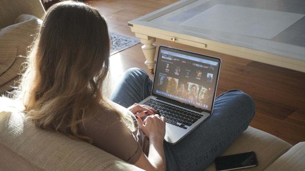 woman in blue denim jeans sitting on couch using macbook pro