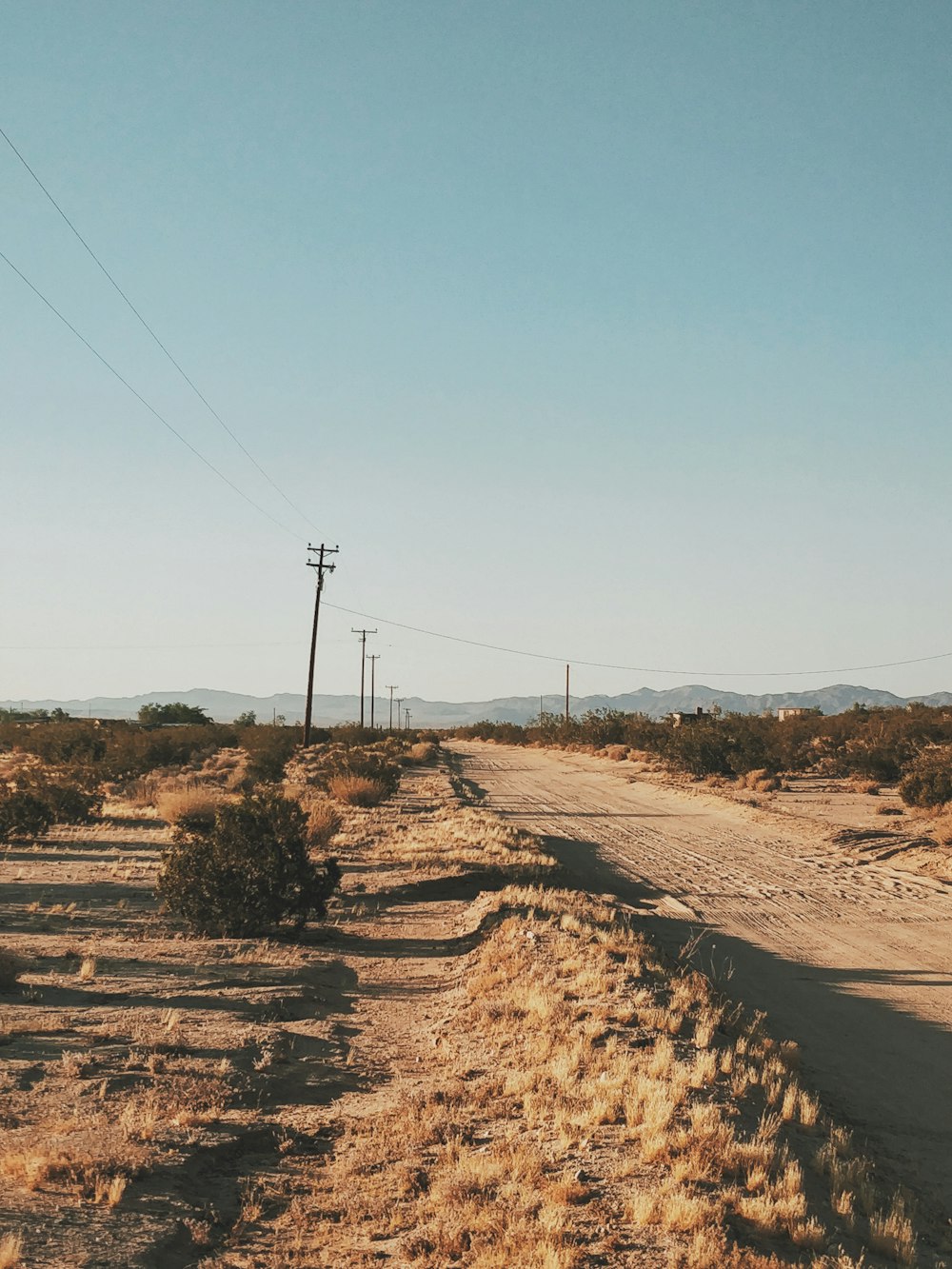 brown dirt road with electric post under blue sky during daytime