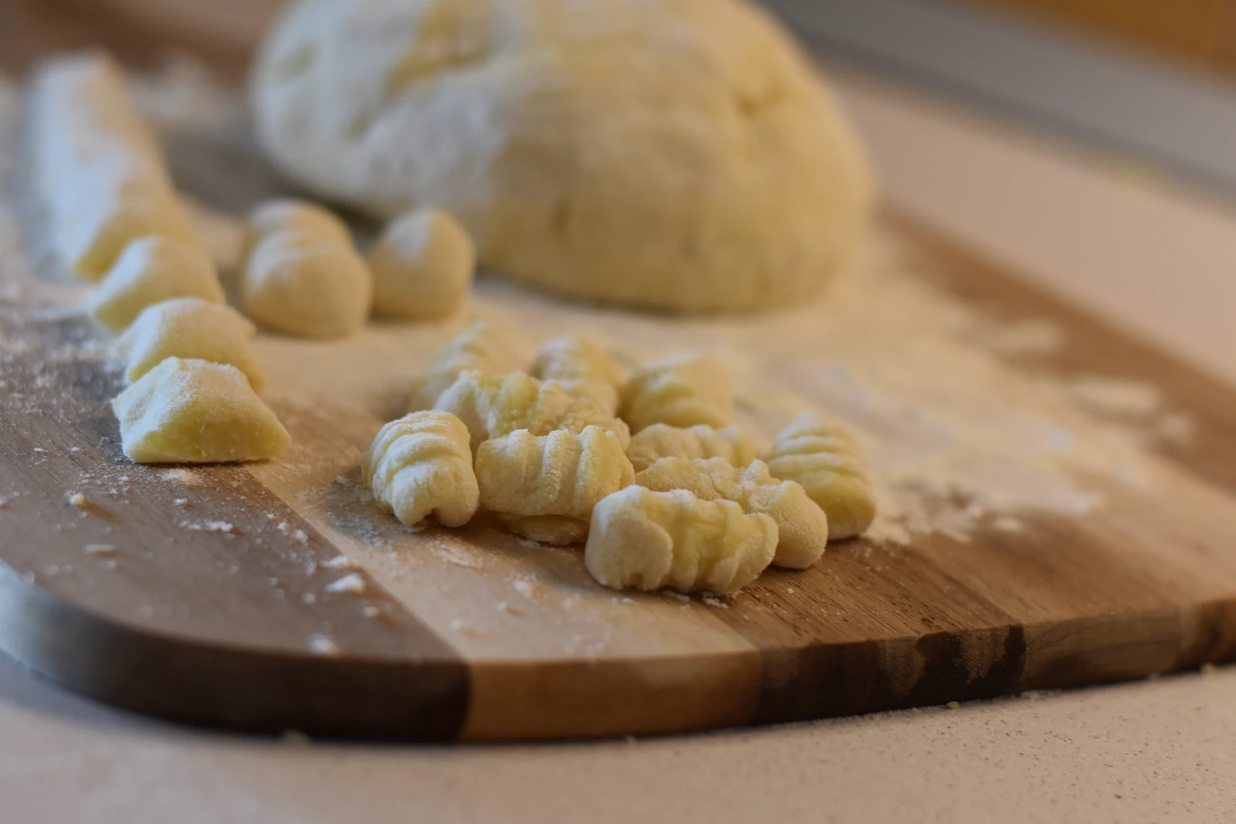 Ridged potato gnocchi beside a ball of their dough on a floured wooden board