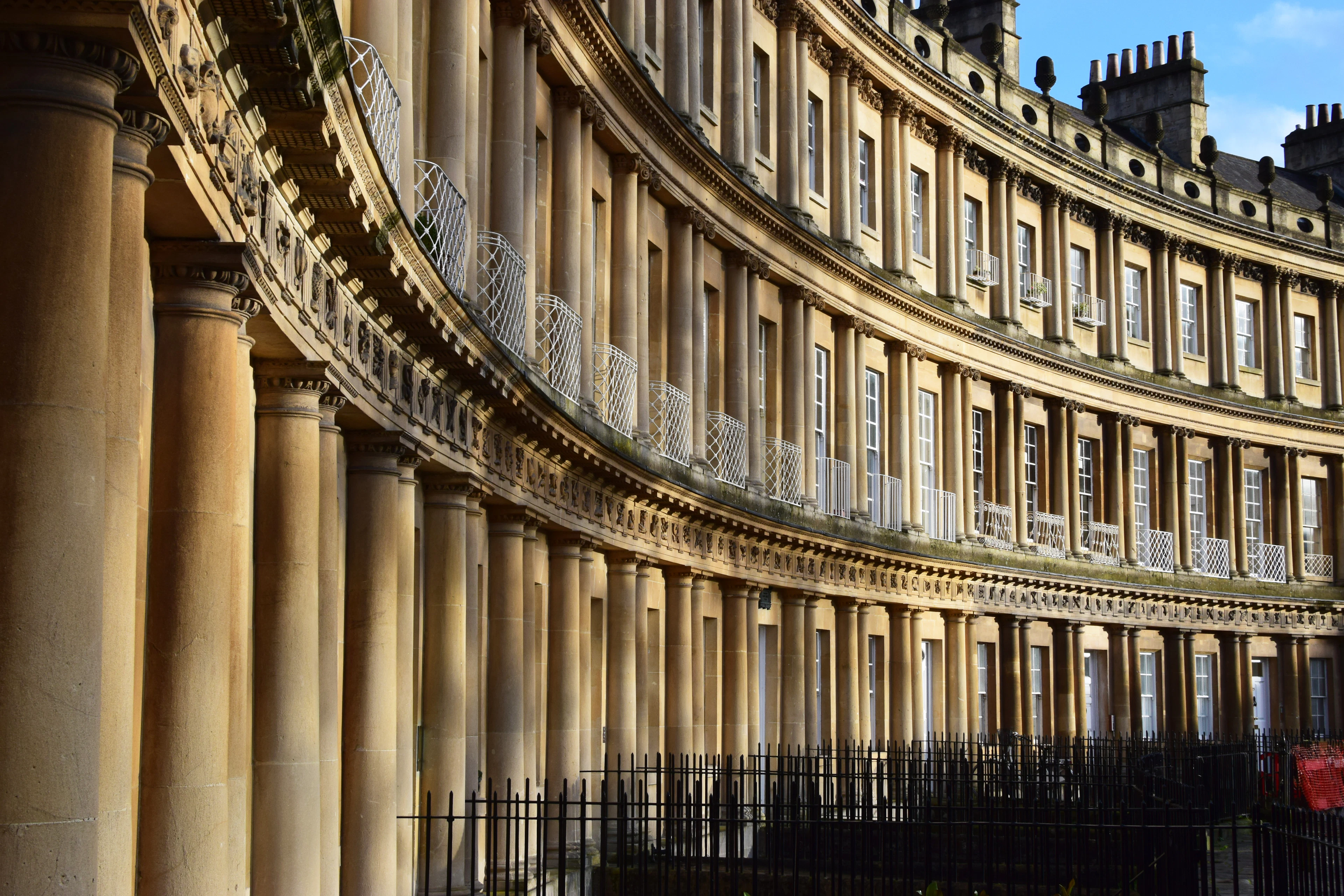 The curved Georgian terrace of The Circus in Bath, its tiers of paired stone columns raked by low golden sunlight above black iron railings.