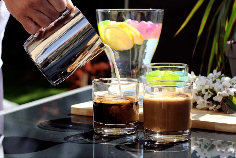 person pouring brown liquid on clear drinking glass