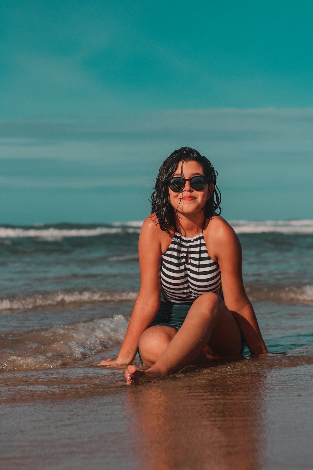 woman in black and white stripe tank top sitting on beach during daytime